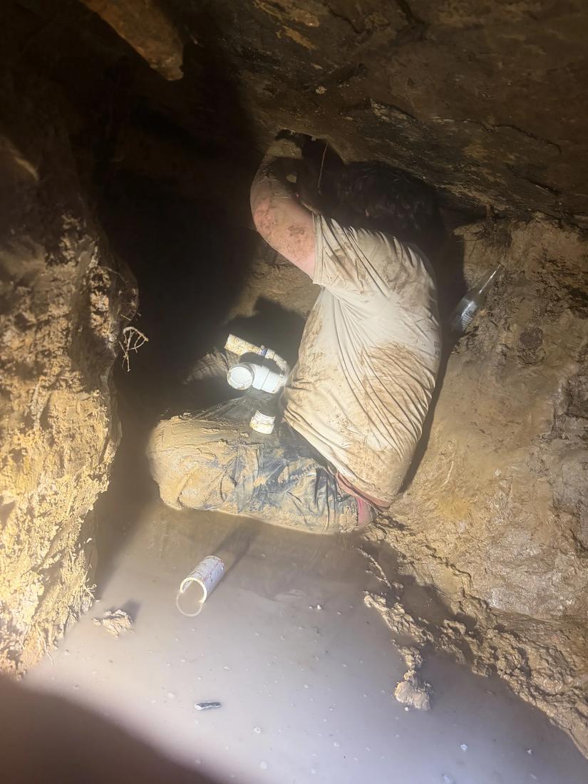 Tech covered in mud working on pipe in a flooded crawlspace
