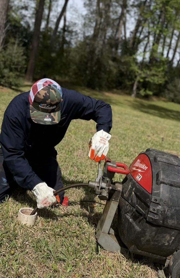 Tech feeding a drain cable into a cleanout with a Milwaukee drum machine